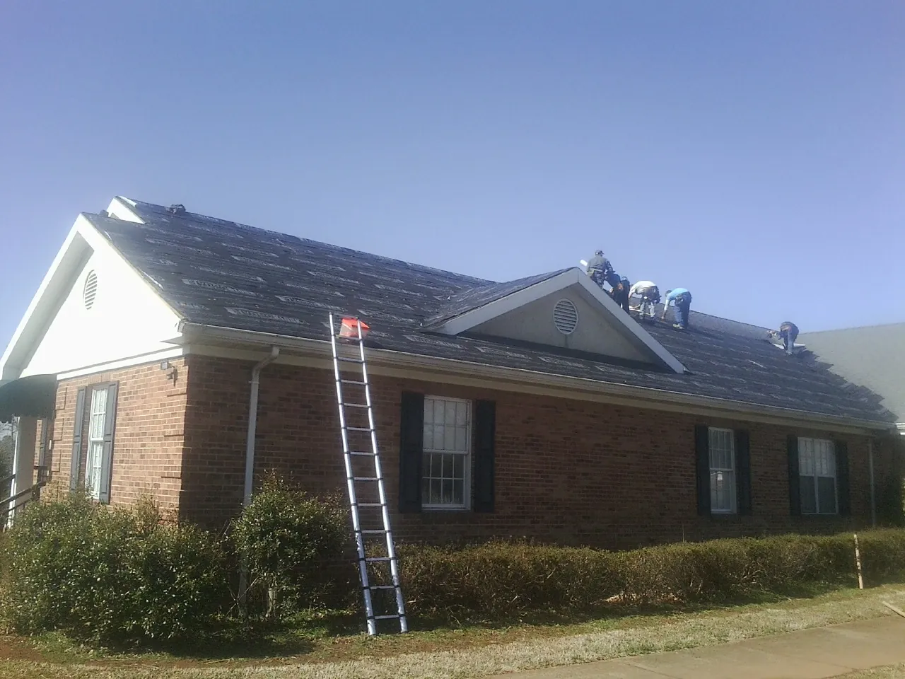 Crew tearing shingles off a brick ranch roof with a ladder set — Metal Roof Repair work by our crew in Horse Shoe
