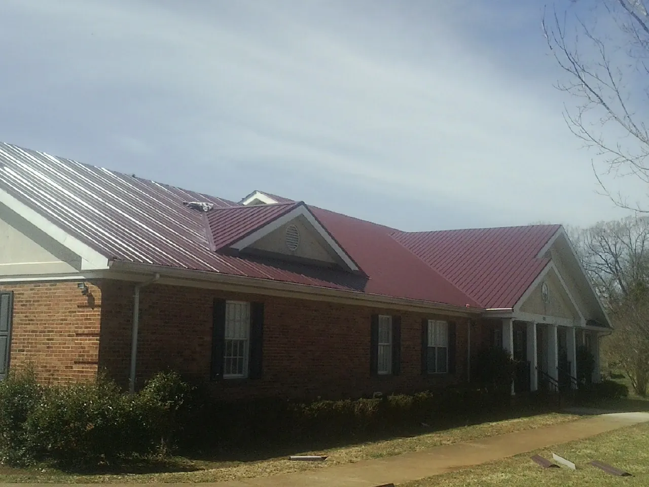 Red metal roof with gabled entries on a long brick building, from a Hail Damage Roof Repair job in Horse Shoe