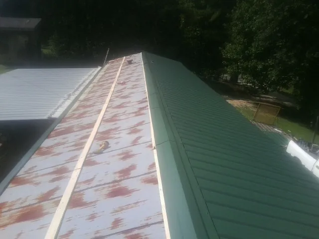 Old rusted panels beside newly installed green metal roofing — Wind Damage Roof Repair by Roofing Brothers in Horse Shoe