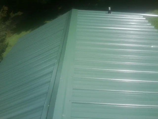 New green metal panels meeting at the ridge of a roof — Flat Roof Repair work by our crew in Horse Shoe