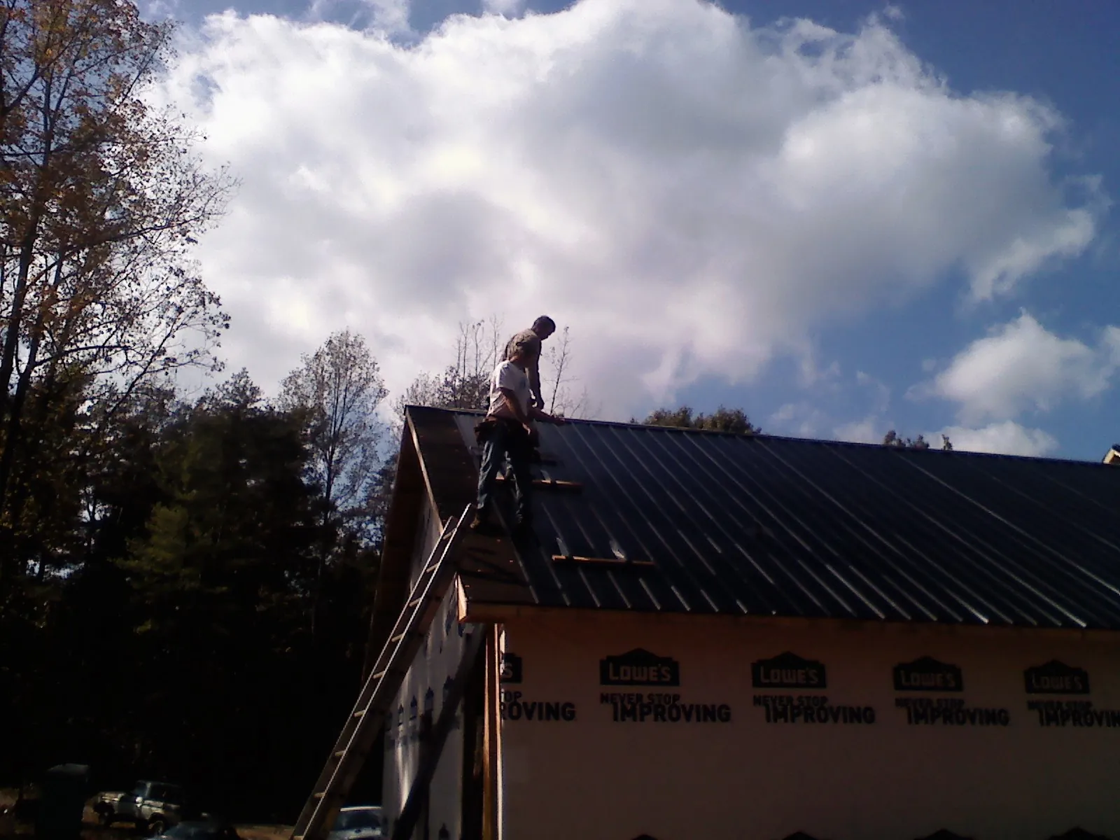 Roofer fastening dark metal panels high against a cloudy sky, from a Roof Inspection job in Horse Shoe