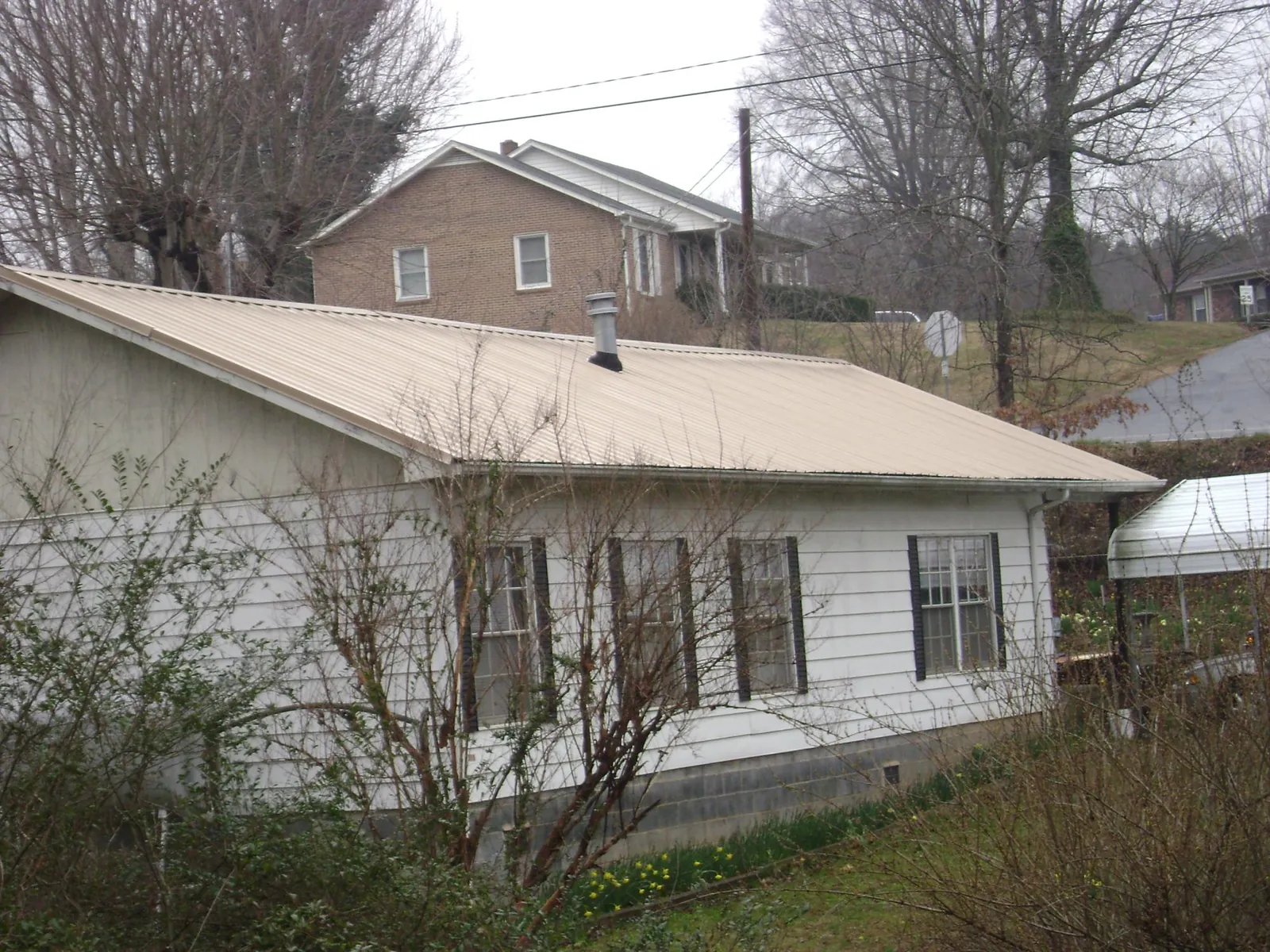 Tan metal roof on a white sided house set into a hillside — Commercial Roofing by Roofing Brothers in Horse Shoe